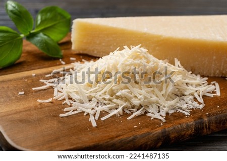 Heap of grated grana padano cheese closeup. Tasty parmesan grated and whole wedge over wooden cutting board. Delicious dairy product. Italian hard cheese. Front view.