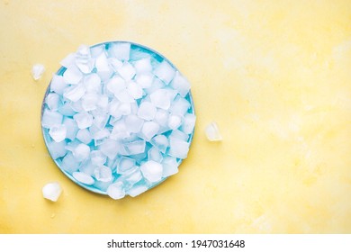 Heap Of Ice Cubes And Crushed Ice On Blue Plate From Above. Yellow  Background. Blank space