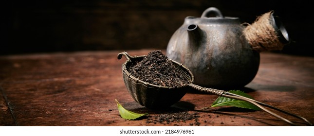 Heap Of Loose Tea On Table With Fresh Green Leaves For Brewing Placed On Wooden Table With Vintage Metal Teapot