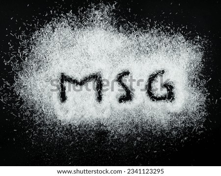 Heap of monosodium glutamate on dark background with text MSG
