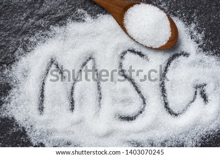 Heap of monosodium glutamate on wooden spoon and dark background with text MSG