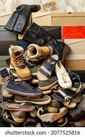 Heap of old, assorted shoes on stacked shoeboxes. Isolated, on the background of an old tattered wall. 