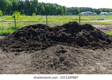 A heap of pure black earth lying in the yard next to the fence. - Shutterstock ID 2311289887