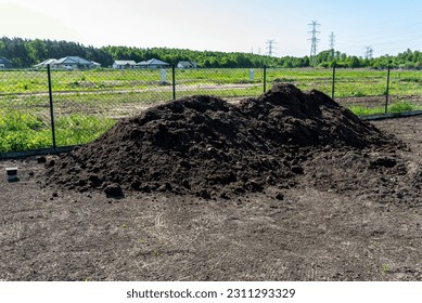 A heap of pure black earth lying in the yard next to the fence. - Shutterstock ID 2311293329