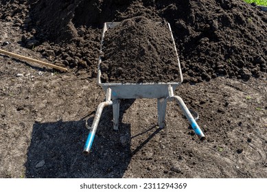 A heap of pure black earth lying in the yard next to the fence, visible shovel and full wheelbarrow. - Shutterstock ID 2311294369