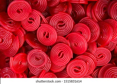 Heap of red strawberry licorice wheels swirl shape candies at supermarket. Creative sweet food confectionery pattern. Kids treats birthday party sugar addiction unhealthy diet concept