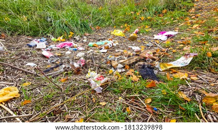 Heap of rubbish on grass in the autumn park.  Plastic and glass bottles, bottle caps and paper. Concept of environmental protection and littering of environment