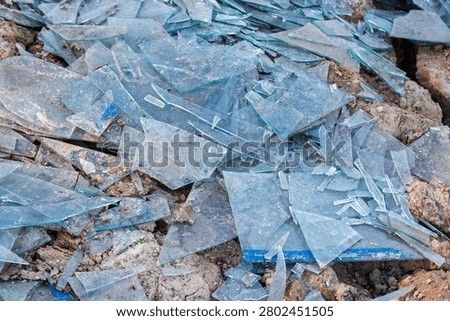 A heap of sharp broken window glass shards discarded as hazardous construction waste on dry cracked earth, showcasing environmental pollution and safety hazards