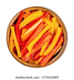 A heap of sliced bell peppers in a wooden bowl. Sweet pepper or capsicum cut in colorful stripes. Fresh yellow, orange and red fruits of Capsicum annuum. Closeup from above, isolated macro food photo.