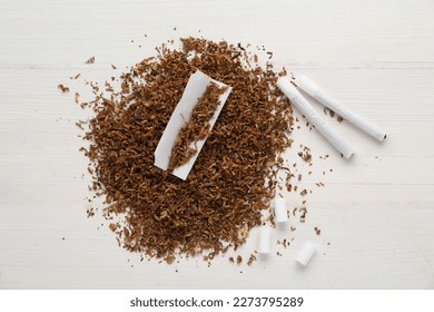 Montón de tabaco, papel, filtros y cigarrillos a mano sobre mesa de madera blanca, tendido plano