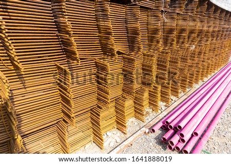 A heap of wiremesh steel covering by rust and pink color plastic pipe on the cocrete floor in front the building in construction