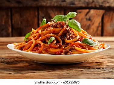 Heaped plate of delicious Italian spaghetti pasta with fresh basil leaves and grated parmesan cheese viewed low angle from the side on a rustic wood table - Shutterstock ID 631925096