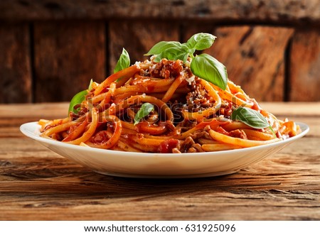 Heaped plate of delicious Italian spaghetti pasta with fresh basil leaves and grated parmesan cheese viewed low angle from the side on a rustic wood table