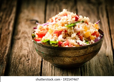 Heaped rustic bowl of savory quinoa with herbs, peppers and tomato for a healthy vegetarian dish rich in protein and nutrients standing on old wooden boards