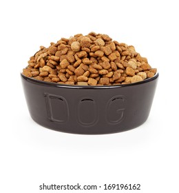 A Heaping Bowl Of Dry Kibble Dog Food In A Black Bowl With The Letters DOG On It. Isolated Against A White Background. 