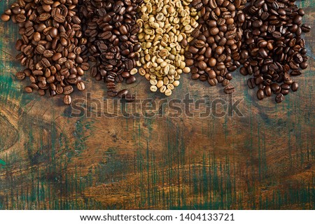 Heaps of assorted raw and roasted coffee beans forming a top border on old vintage stained wood with copy space viewed from above