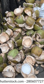 Heaps of split green coconuts with white inner flesh and brown husk remnants fill a bin, showing varied sizes and rough exteriors under natural light.