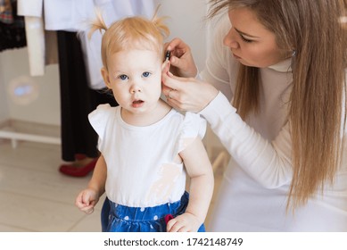 Hearing Aid In Baby Girl's Ear. Toddler Child Wearing A Hearing Aid At Home. Disabled Child, Disability And Deafness Concept.