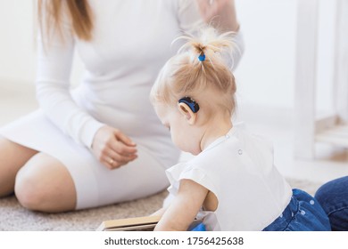 Hearing Aid In Baby Girl's Ear. Toddler Child Wearing A Hearing Aid At Home. Disabled Child, Disability And Deafness Concept.