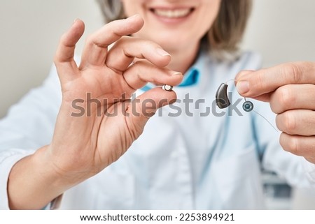 Hearing aid battery replacement. Positive audiologist showing hearing aid and battery for it, holding them in her hands in front of him