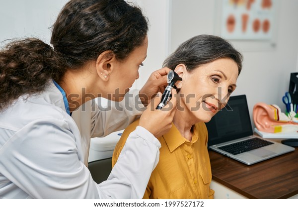 Hearing exam for elderly citizen people.\
Otolaryngologist doctor checking mature woman\'s ear using otoscope\
or auriscope at medical\
clinic