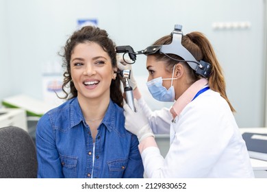 Hearing exam. Otolaryngologist doctor checking woman's ear using otoscope or auriscope at medical clinic. Otorhinolaryngologist pulling ear with hand and looking at it with otoscope closeup. - Powered by Shutterstock