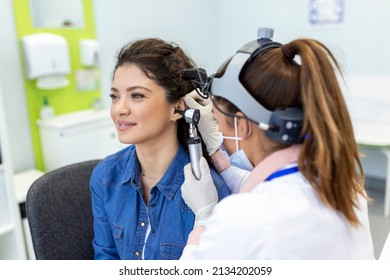 Hearing exam. Otolaryngologist doctor checking woman's ear using otoscope or auriscope at medical clinic. Otorhinolaryngologist pulling ear with hand and looking at it with otoscope closeup. - Powered by Shutterstock