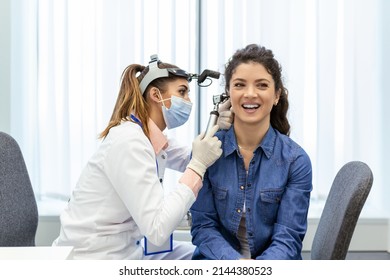 Hearing exam. Otolaryngologist doctor checking woman's ear using otoscope or auriscope at medical clinic. Otorhinolaryngologist pulling ear with hand and looking at it with otoscope closeup. - Powered by Shutterstock