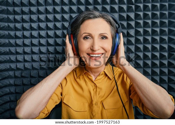 Hearing loss treatment. Positive mature woman\
wearing audiometry headphones while hearing test and audiogram in\
special audio room