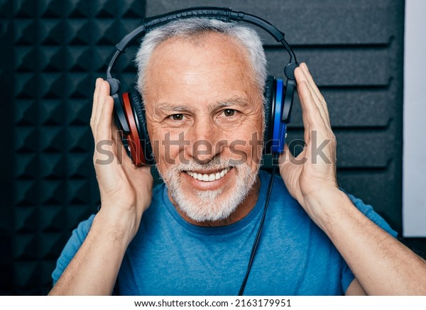 Hearing loss treatment. Positive senior man wearing\
audiometry headphones while hearing test and audiogram in special\
audio room