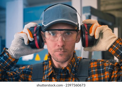 Hearing protection. A factory worker puts on noise-cancelling earmuffs. Work safety theme. - Powered by Shutterstock