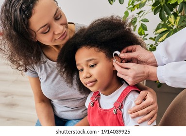 Hearing treatment for a child. African American girl with her mother during installation hearing aid by her audiologist