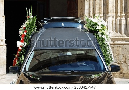 Hearse or funeral car outside a church, with wreaths and bouquets on both sides
