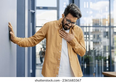 Heart attack, chest pain in young businessman overworked man outside office building holding hands to chest in pain.