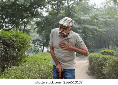 Heart attack concept. Indian Senior man suffering from chest pain outdoor in park. Asian senior male having health issues and body pain suddenly in garden - Powered by Shutterstock