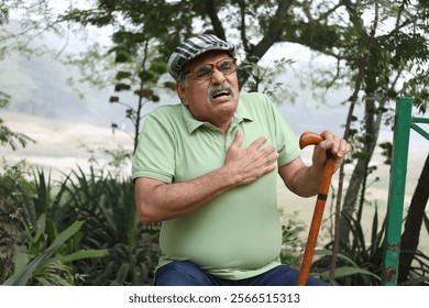 Heart attack concept. Indian Senior man suffering from chest pain outdoor in park. Asian senior male having health issues and body pain suddenly in garden - Powered by Shutterstock