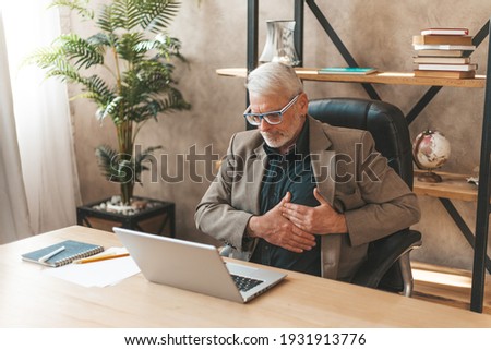 Heart attack at work in the office. Senior man holding his sternum with his hands, pain and discomfort.