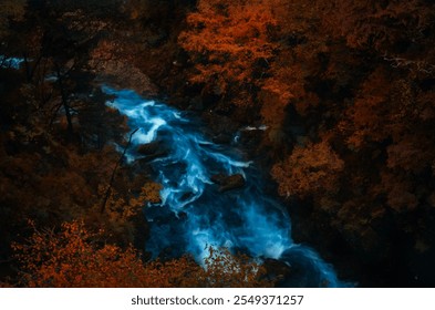 In the heart of autumn, a vibrant river cuts through a dense forest ablaze with fiery red and orange hues. The rushing water glows in surreal blue tones, contrasting sharply against the warm colors of - Powered by Shutterstock