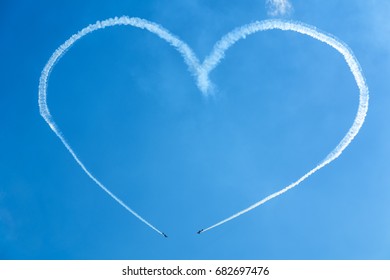 A heart in the blue sky from two skywriting small planes at an air show. Symbol of love in the heaven. Trail of an airplane in the shape of a big heart.