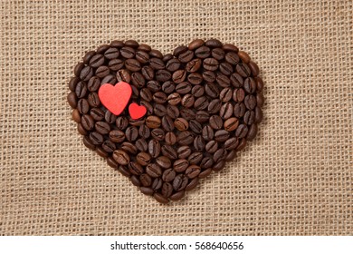 Heart of coffee beans with red hearts on sackcloth.