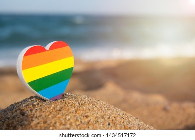 Heart Of The Color Of The Gay Flag On The Sand With The Sea On Background. LGBT Concept. Gender Equality Concept. Copy Space. Romantic Trip Gay Honeymoon. Same-sex Couple. 