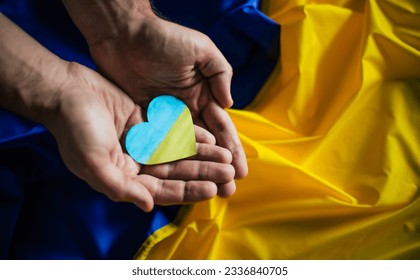 Heart in the colors of the flag of Ukraine in hands on flag background. Ending the war in Ukraine. Help and support. Strong nation. Battle for justice, freedom and democracy. - Powered by Shutterstock