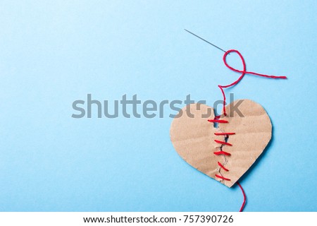 The heart is combined, love is back. A paper heart made of two halves is sewn with a red thread with needle
on a blue background