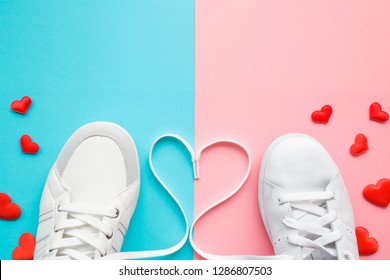 Heart created from white shoelaces between male and female sport shoes. Bright, red hearts. Love concept. Empty place for lovely, cute text, quote or sayings on pastel blue and pink paper. Closeup.