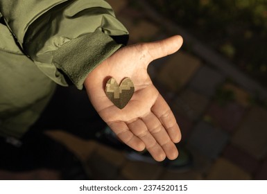 heart cut from camouflage fabric on child palm illuminated by sun. Stop war in Ukraine. With love and gratitude to soldiers of armed forces. Experiences of Ukrainian children due to military actions