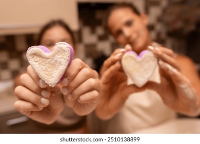 Heart Dough Kitchen Mom Daughter Baking - Two women, a mother and daughter, are baking heart-shaped dough in a kitchen. They are holding their creations in their hands, smiling at the camera. - Powered by Shutterstock