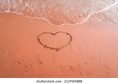 A Heart Drawn With Fingers On The Red Beach. The Waves Are About To Wash Over. Top View. Midday On The Pacific Coast. Valentine's Day. Romantic Concept.love Heart Shape