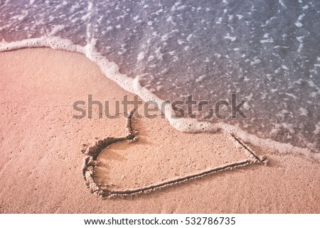 Heart drawn on the beach sand being washed away by a wave. Love affair, summer love or breakup and divorce concept. Ephemeral romantic love. Not true love. End of relationship.