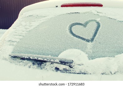 Heart drawn on a car windshield  covered with fresh Christmas snow.