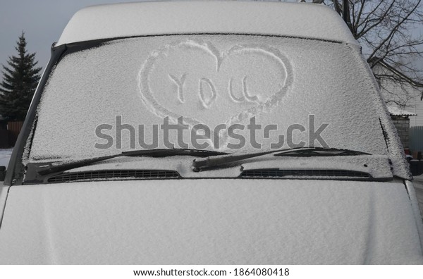 Heart\
drawn on a car windshield covered with fresh Christmas snow. \
Windscreen wipers and a snow covered car or bus.winter season.\
front view. happy Valentines day. 14th\
february